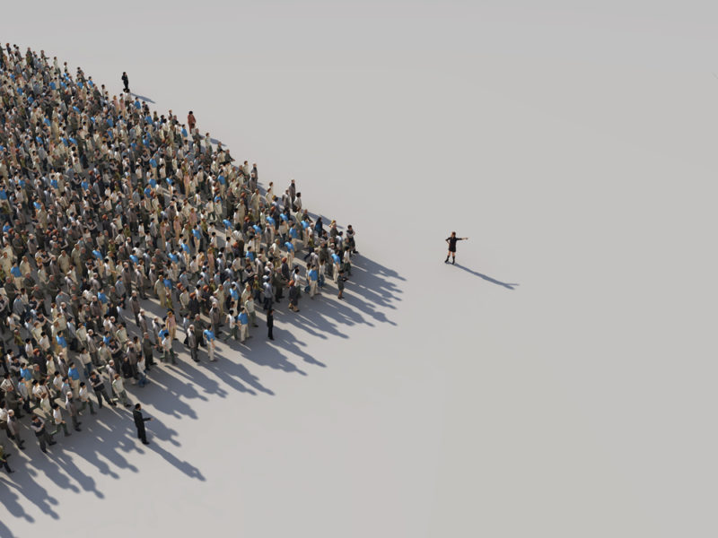 A large dense group of people standing together, forming a triangular shape, the tip of which points to their leader, a single individual standing a short distance away who points to an unseen point in the distance beyond the frame of the photo.